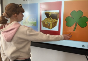 Dziewczynka wybiera odpowiednią nazwę „shamrock” na tablicy multimedialnej podczas zajęć z okazji Dnia Świętego Patryka.